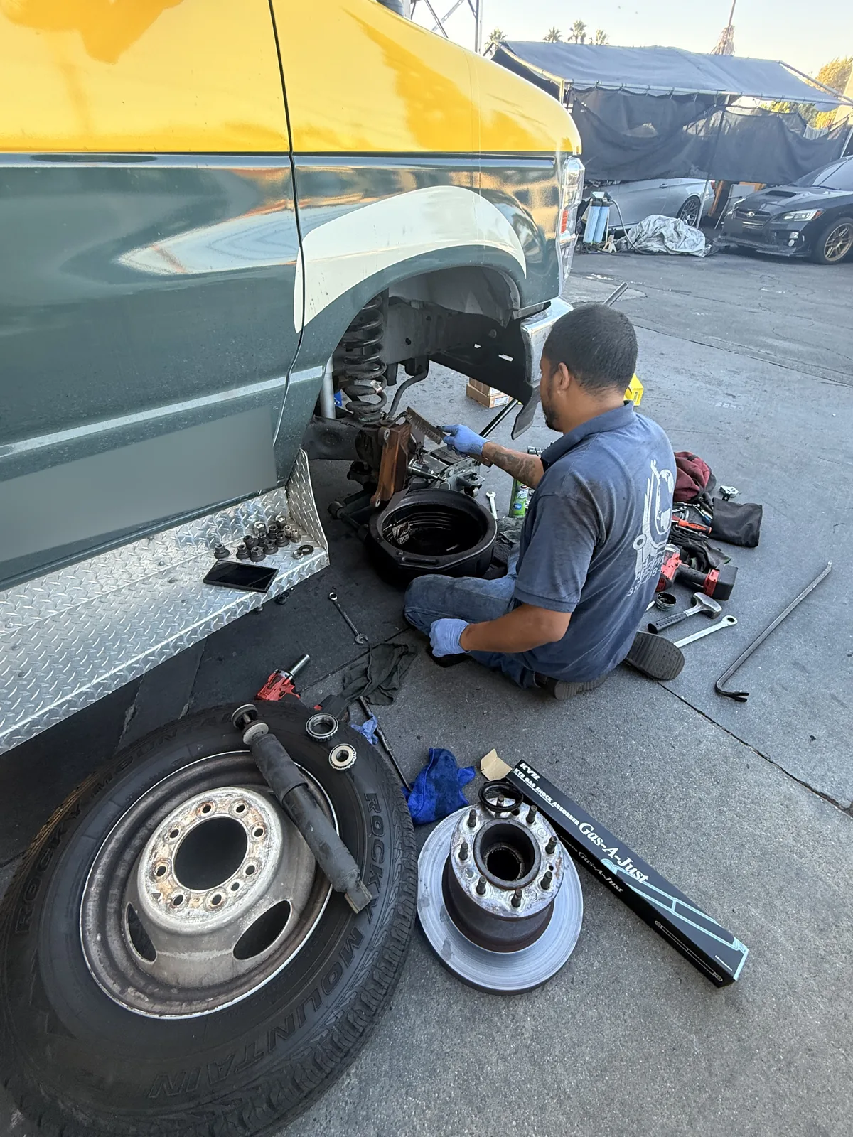 Technician working at a small commercial bus’s exposed front wheel assembly.