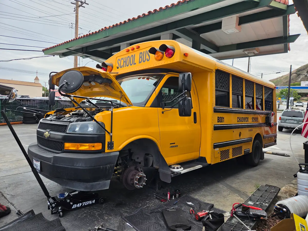 School bus at Hillside Auto Repair with its hood open and front wheel removed